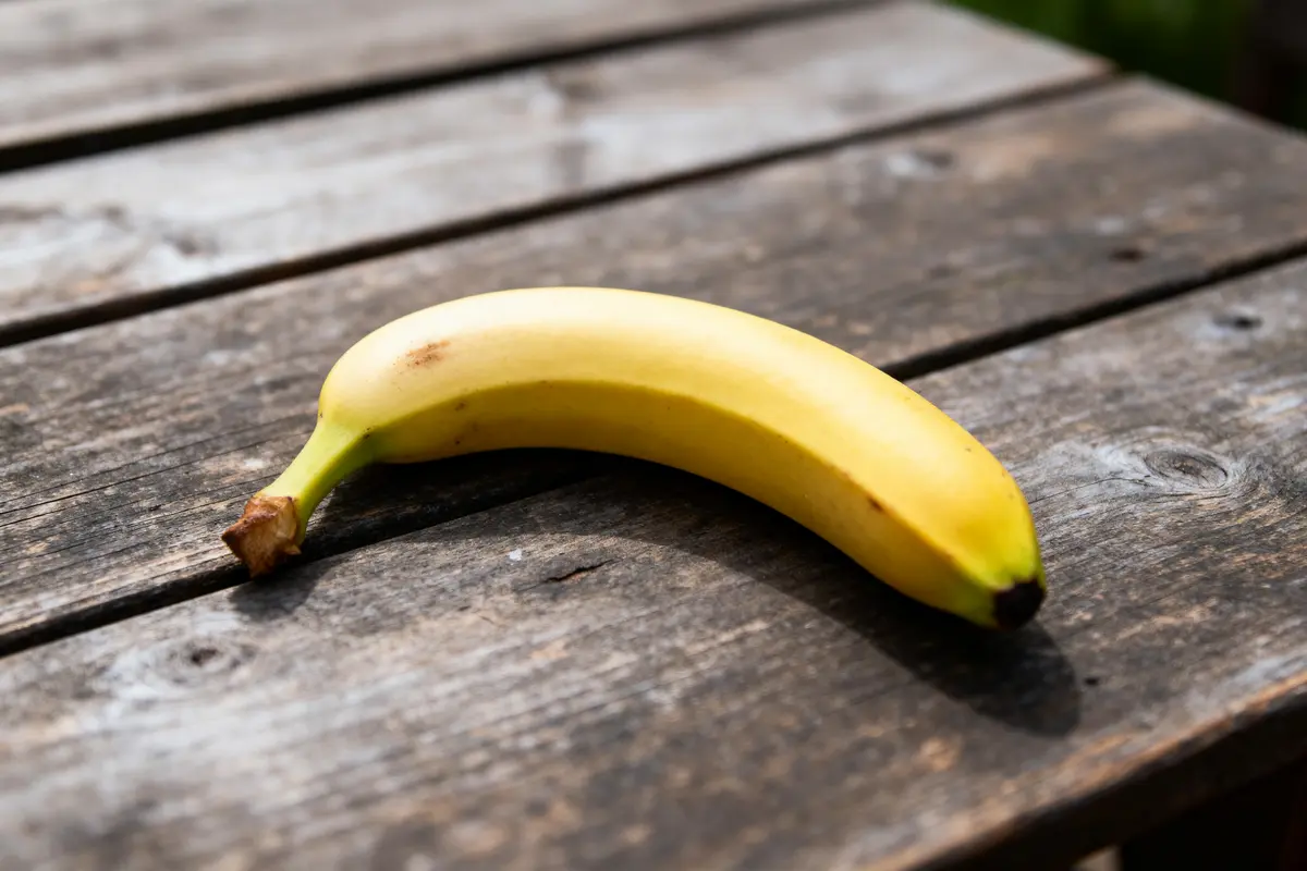 Banane jaune posée sur une table en bois, éclairage naturel, ombre visible.
